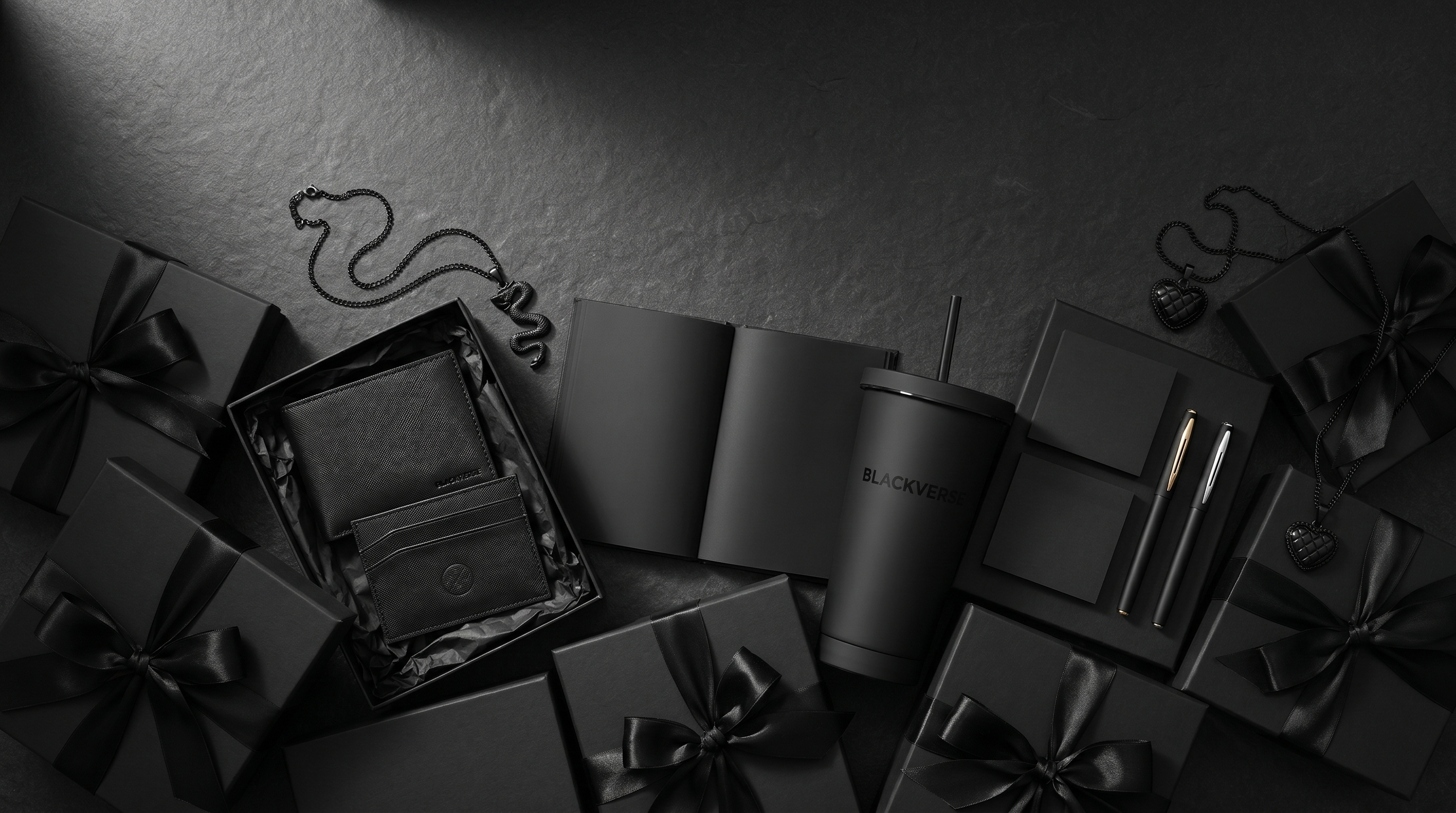 An abundant all-black gift arrangement — matte-black gift boxes with satin ribbons, a wallet, notebook, tumbler, and pendants on dark stone — BLACKVERSE gift guide